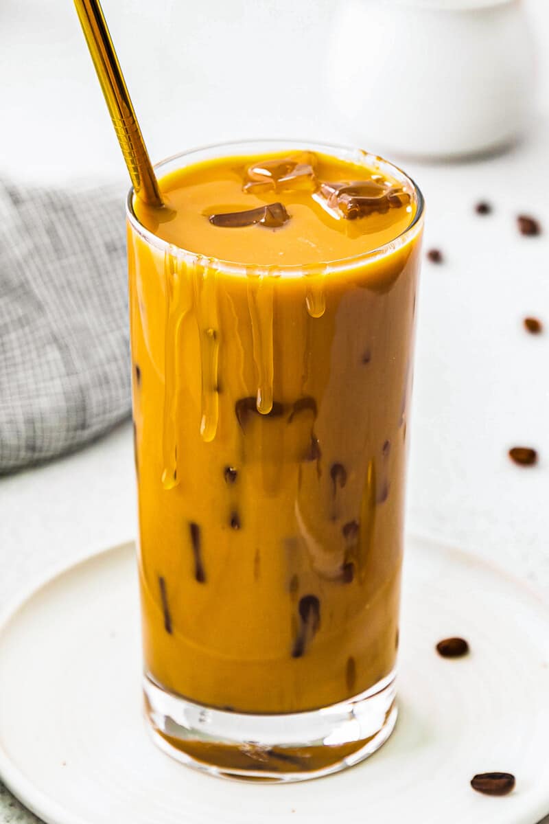 up close stirred iced caramel latte in glass with gold straw