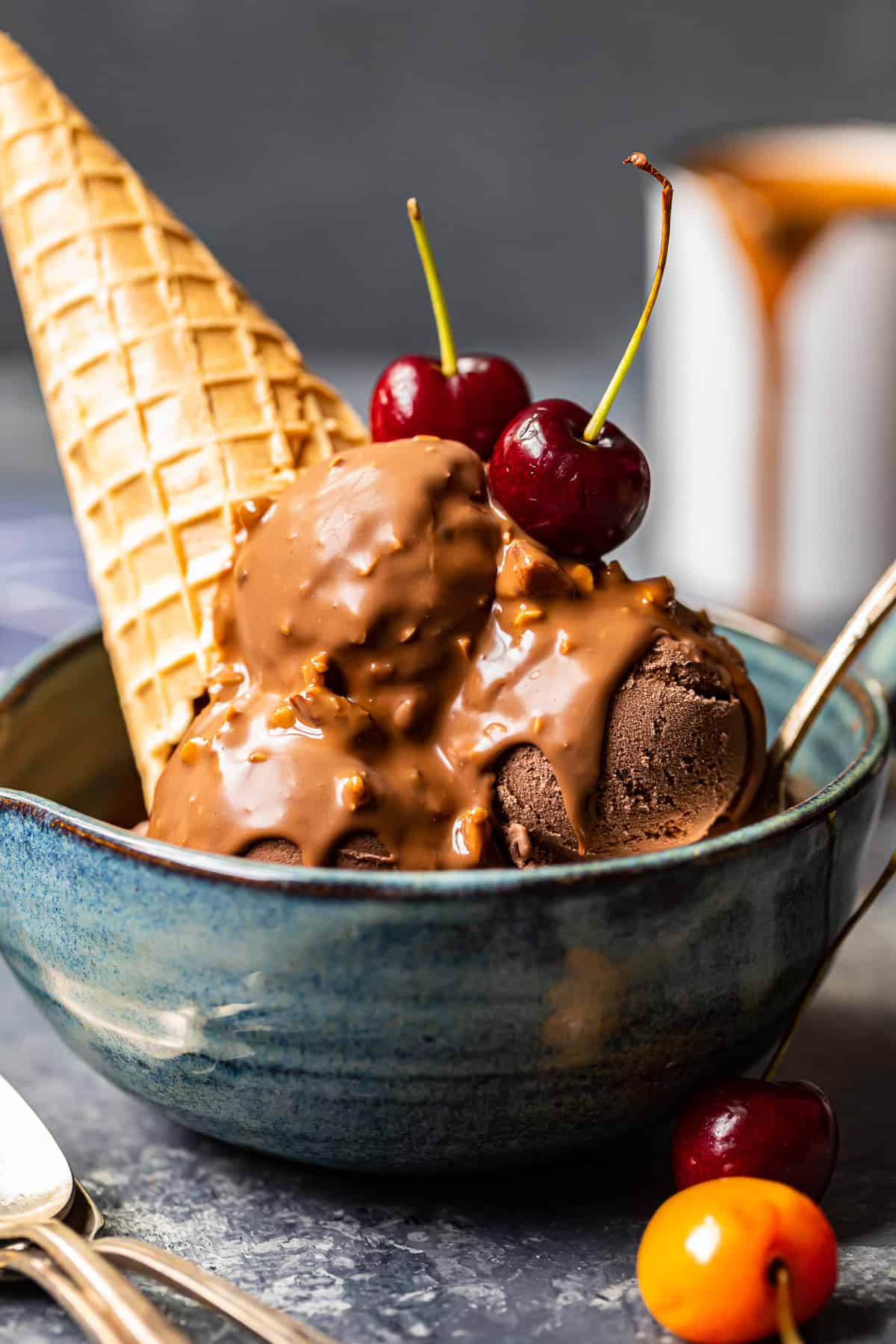 chocolate ice cream scoops topped with symphony bar chocolate shell and cherries in a blue bowl with a spoon