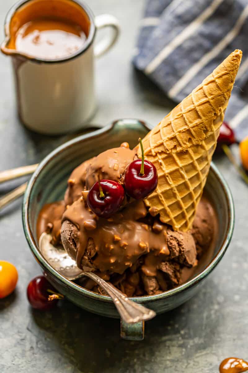 chocolate ice cream scoops topped with symphony bar chocolate shell and cherries in a blue bowl with a spoon