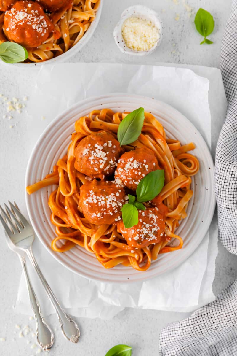 overhead view of chicken parmesan meatballs over spaghetti in a white bowl with 2 forks.