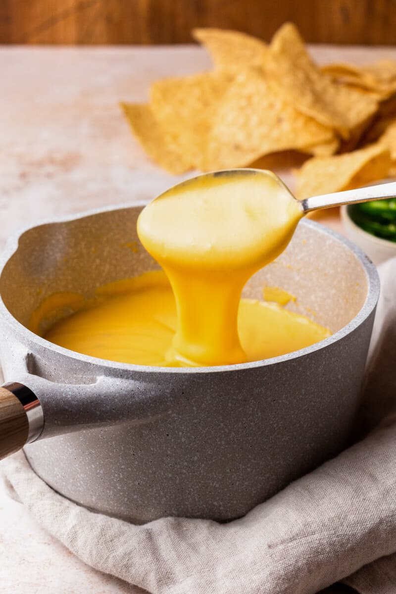 Nacho Cheese Sauce is something everyone should be able to make. An easy cheese dip (made in 5 minutes!) always comes in handy! This homemade nacho cheese sauce recipe is so delicious and so quick. Make it in a flash, dip in some chips, or use this versatile cheese sauce on all kinds of recipes! spoon dipping into a pot of cheese sauce